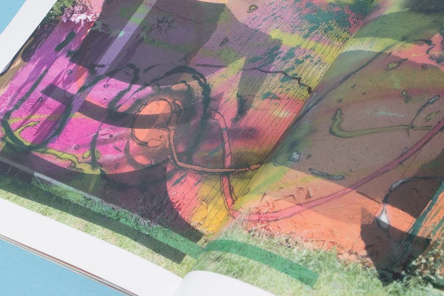 Catapum abierto sobre fondo azul: doble página con un muro pintado en rosas, amarillos y verdes