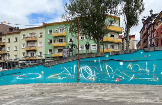 Mural de trazos libres blancos y de colores sobre fondo turquesa en un muro de contención. Cama elástica, Disfrute y Tropiezo, Oviedo 2021.