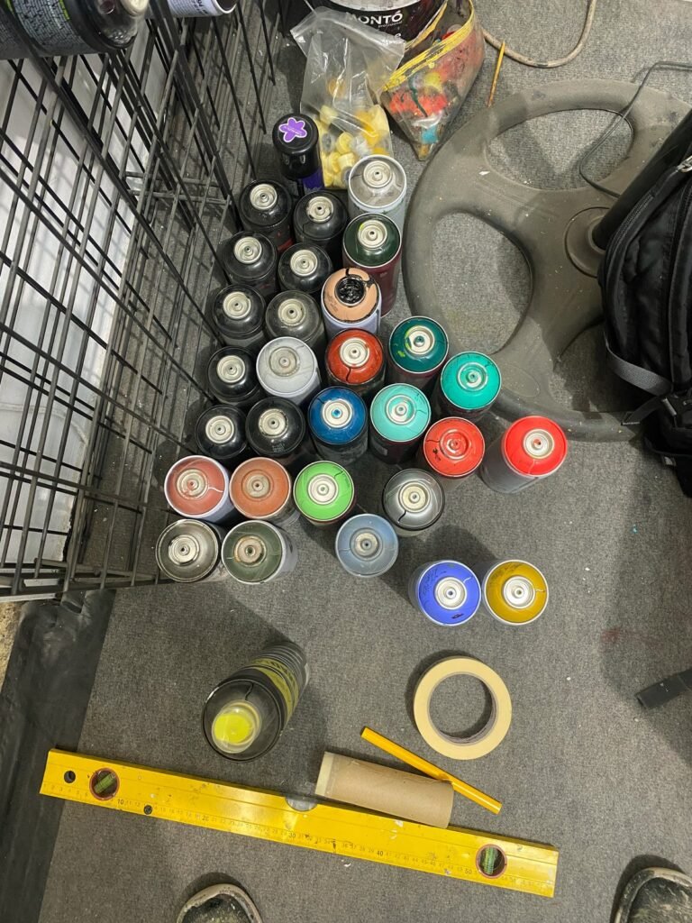 Botes de spray usados y recuperados en el suelo del taller, junto a un nivel amarillo y cinta de carrocero.