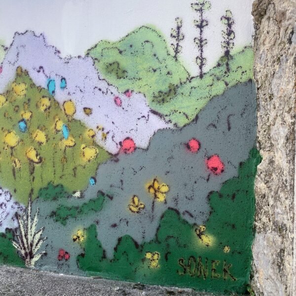 Detalle del mural: flores amarillas de tres pétalos y la firma SONEK junto a un pilar de piedra