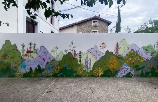 Mural de vegetación pintado con plástica y spray en un muro exterior bajo y alargado, bajo las ramas de un árbol