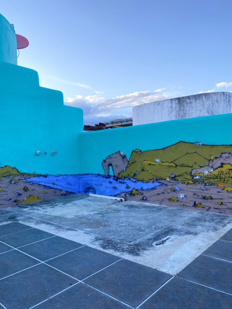 El muro al atardecer, con el arco de roca y el mar azul pintados en su base y el cielo despejado.