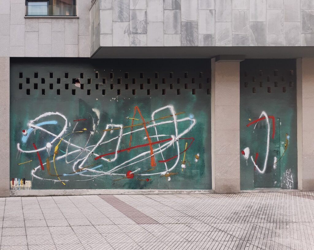 Persiana de un local de Oviedo pintada con trazos blancos, azules, amarillos y rojos sobre fondo verde