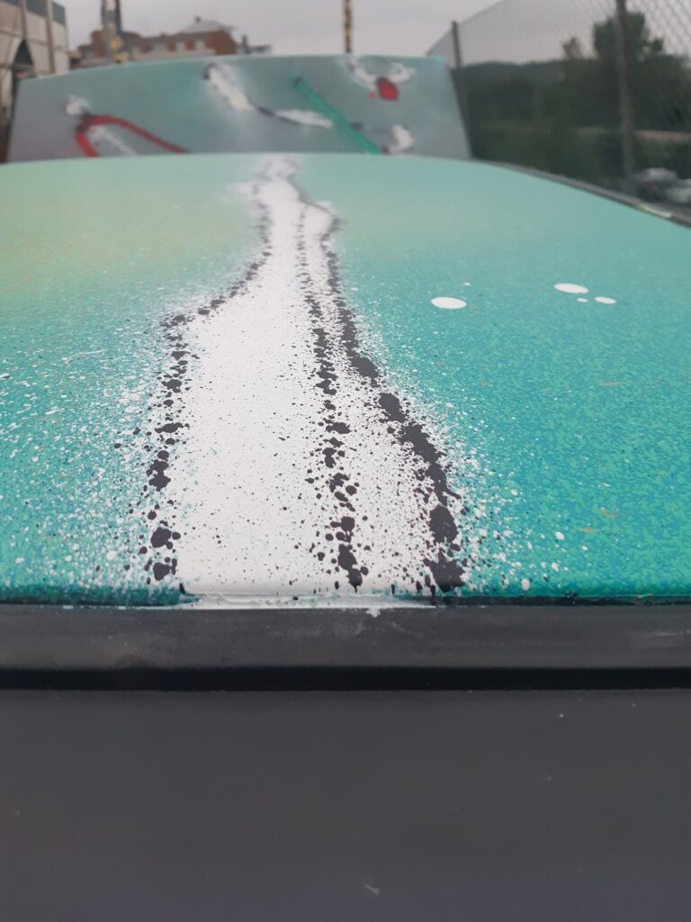 Detalle de una franja blanca con salpicaduras negras sobre la chapa verde