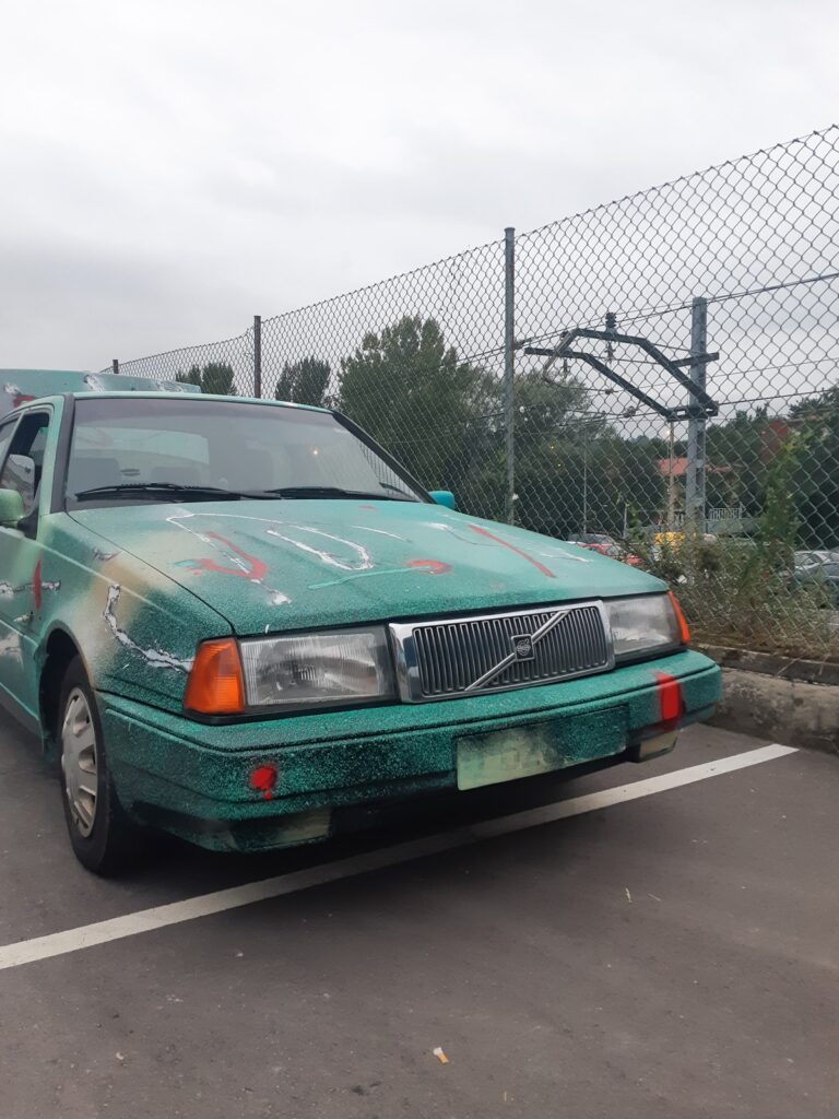 El coche pintado en un aparcamiento junto a una valla metálica, bajo un cielo nublado