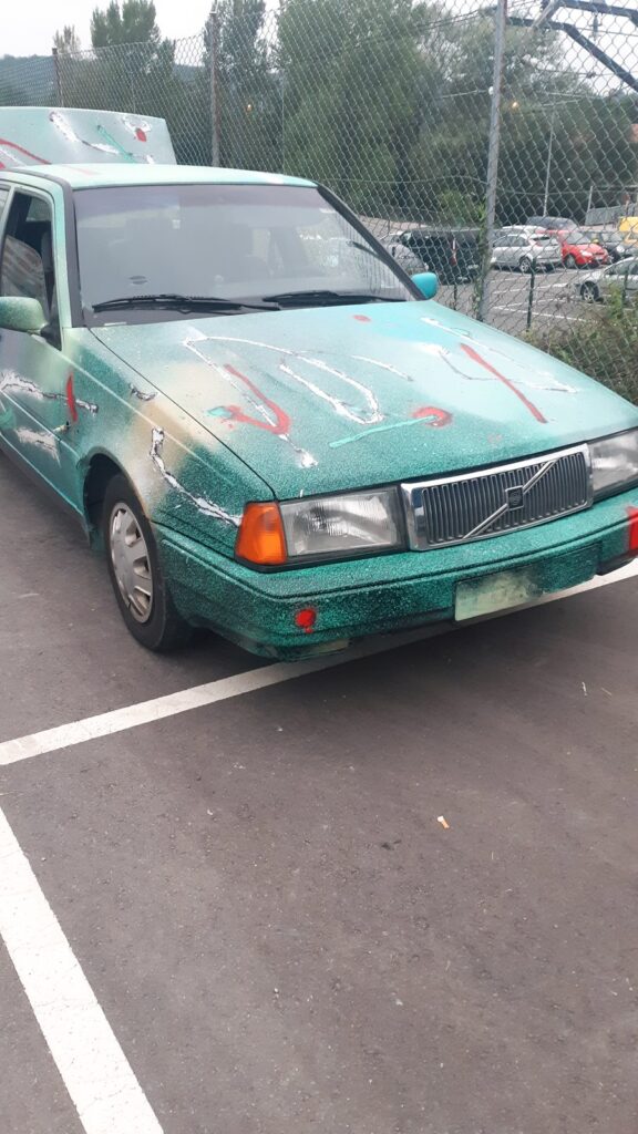 El coche pintado visto desde arriba en el aparcamiento, con trazos blancos y rojos sobre el capó verde