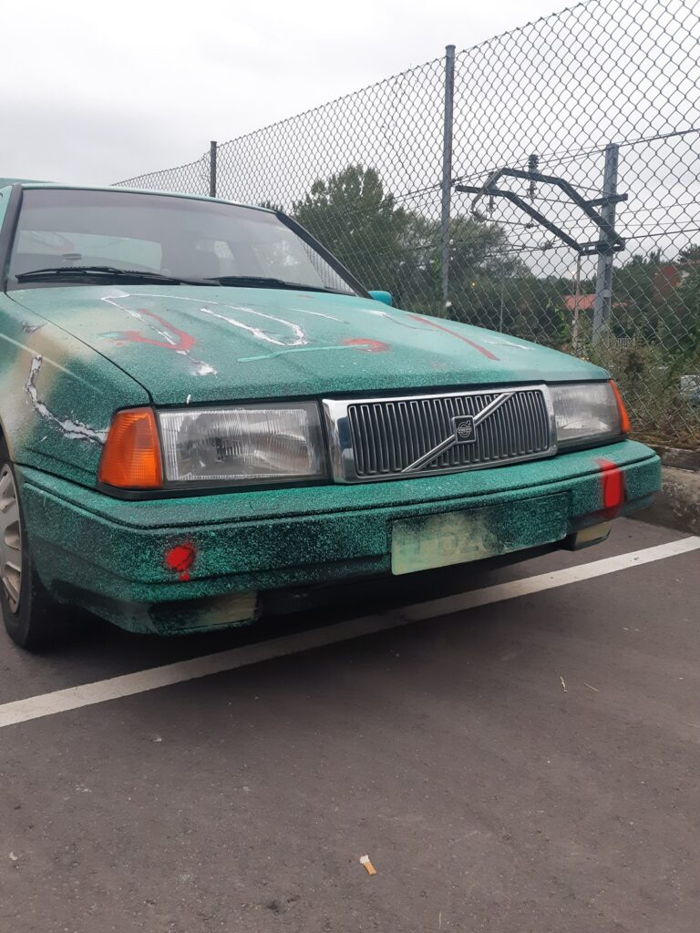 Frontal del coche pintado de verde con salpicaduras, con trazos blancos y rojos sobre el capó