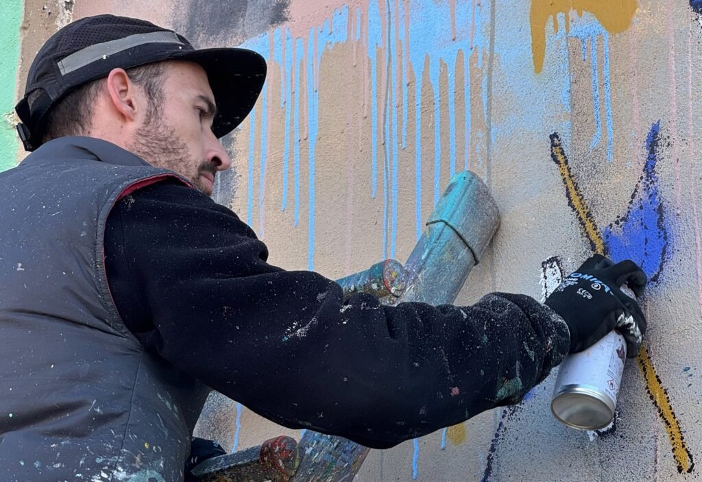 Sonek pinta con spray un muro con chorreones azules y trazos amarillos.