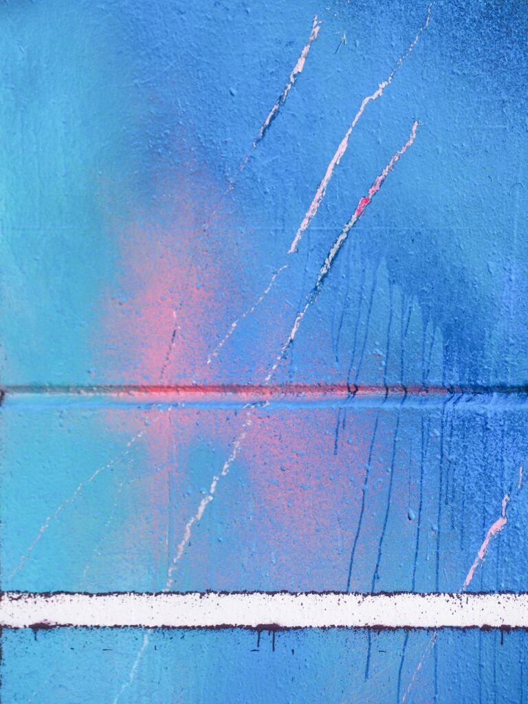 Detalle en vertical: un brillo rosa bajo la capa azul, arañazos blancos, la junta del muro y la línea blanca
