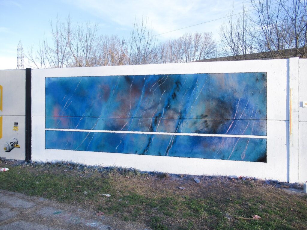 El mural visto en diagonal, con su marco blanco y los pilares del muro, delante de árboles sin hoja