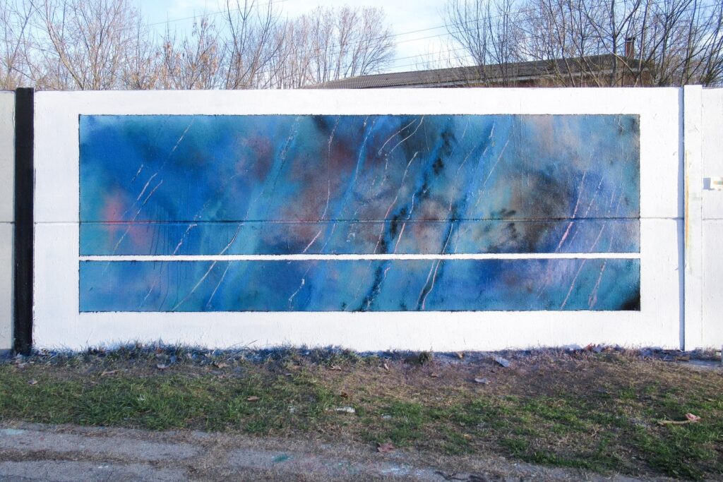 Mural abstracto de spray en azules, con rosas, negros y arañazos blancos, pintado dentro de un marco blanco en un muro de hormigón, visto de frente