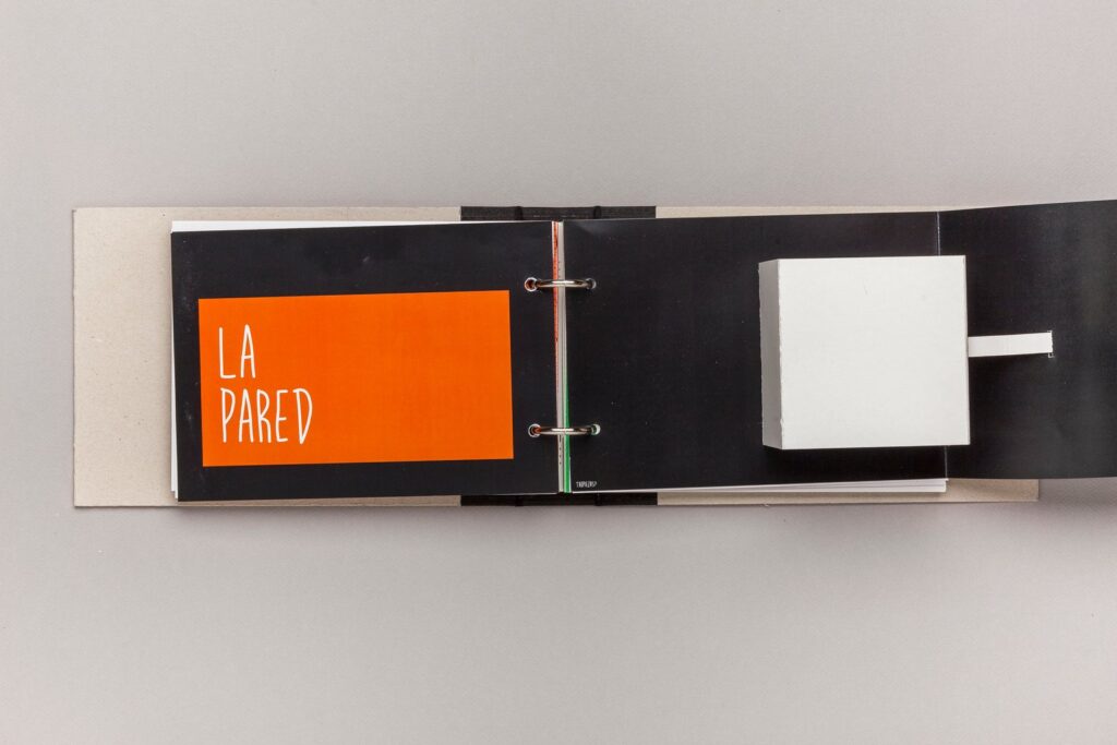 Apertura del capítulo «La pared», en naranja sobre negro, con una caja blanca desplegable en la página de al lado