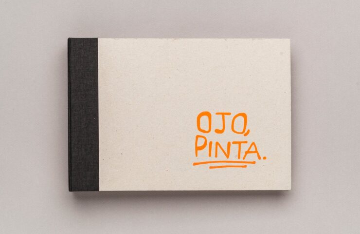 Cubierta de Ojo, Pinta!: cartón gris con lomo de tela negra y el título escrito a mano en naranja