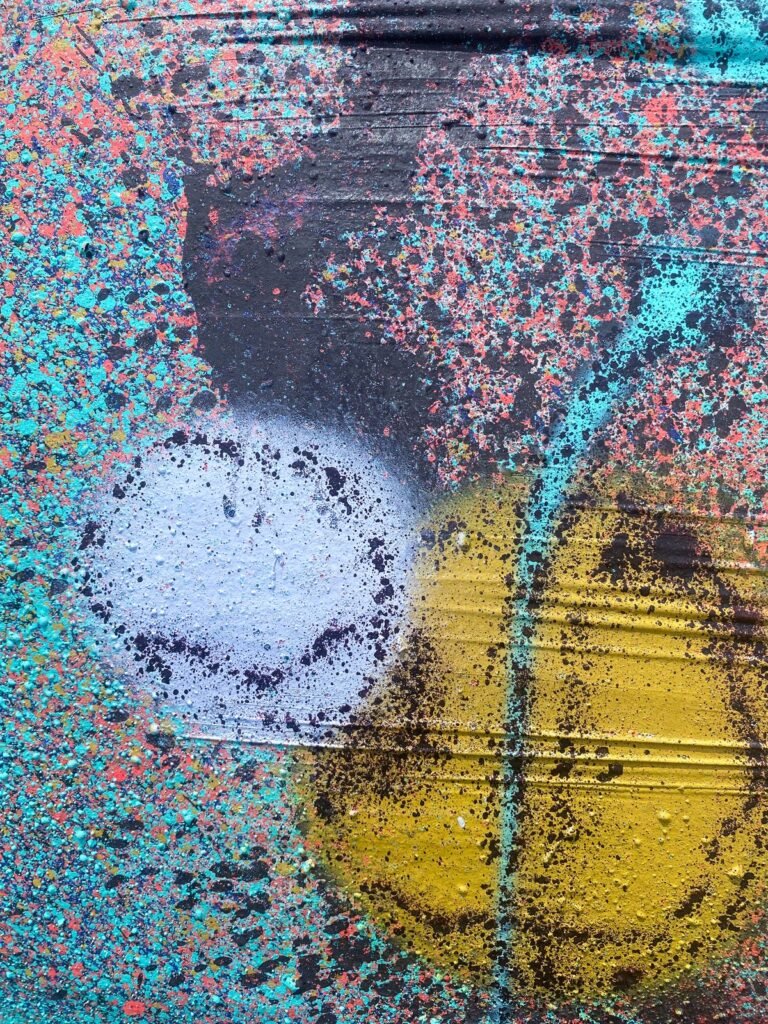 Detalle de la superficie de una bola: blanco y amarillo entre salpicaduras de spray, con las arrugas del plástico visibles.