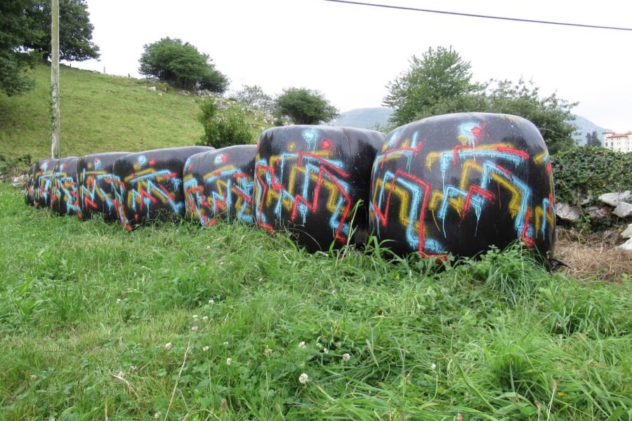 Una fila de bolas de silo negras, pintadas con trazos en turquesa, amarillo y rojo, en un prao de Porrúa.