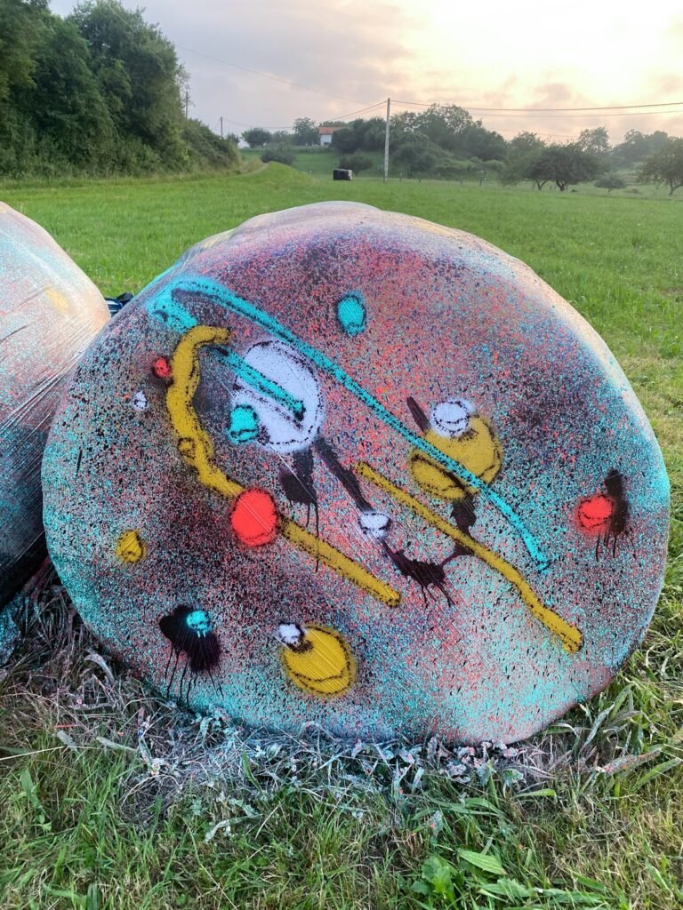 La cara circular de una bola de silo con amarillo, blanco, rojo y trazos turquesa y negros sobre un fondo turquesa y rosa.