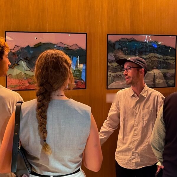 Nacho explicando la serie a una pareja de espaldas, con la sala completa detrás, en el vernissage de "Allí donde quiero estar" en el Hotel Ocean Drive