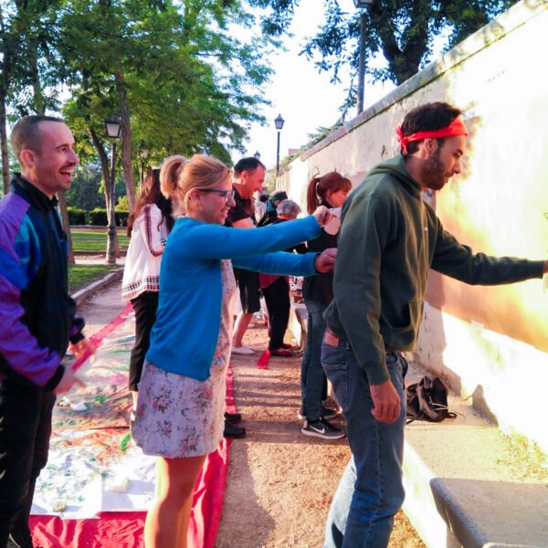 Participantes pintan un muro en un parque al atardecer; uno de ellos dibuja una figura en la pared.