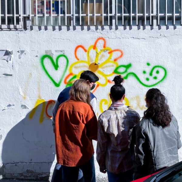 Alumnado de New York University en Madrid pinta con spray un corazón y una flor en una pared blanca.