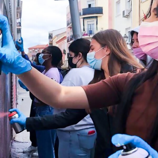 Alumnas de New York University en Madrid, con mascarilla y guantes, pintan con spray una pared de la calle.