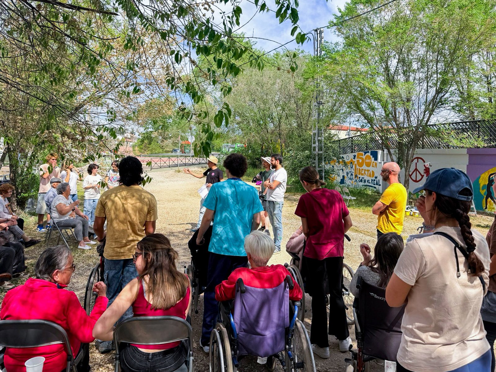 Jóvenes y mayores, algunos en silla de ruedas, escuchan en corro la explicación antes de empezar a pintar.