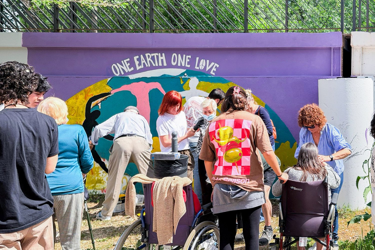 Jóvenes y mayores, algunos en silla de ruedas, pintan juntos el mural One Earth One Love en Soto del Real.