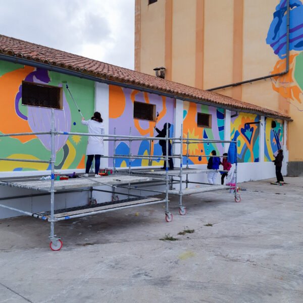 La nave de Titanes en La Solana a medio pintar en color, con andamios y participantes pintando desde ellos.