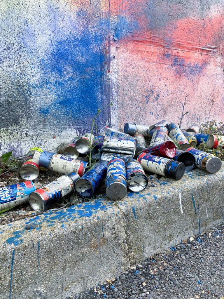 Botes de spray usados, recogidos de otros talleres, amontonados al pie del muro