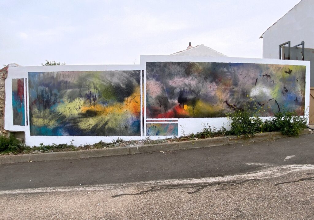 Mural abstracto de spray en azules, amarillos, rosas y rojos sobre un muro blanco de calle, visto de frente