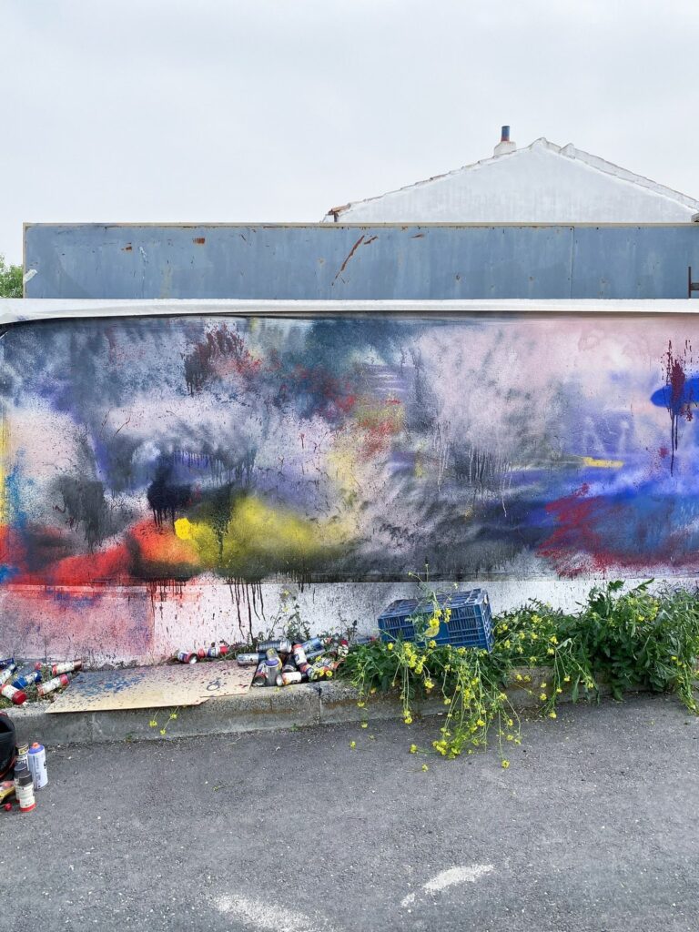 Primeras capas de spray de colores sobre el muro, con botes de pintura al pie