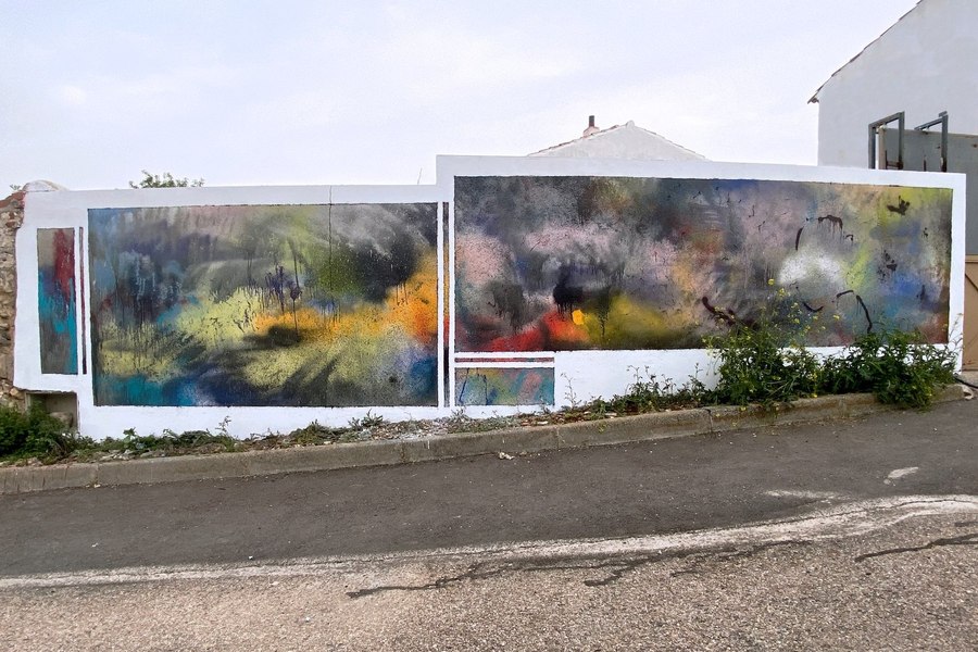 Dos paneles de pintura abstracta a spray, enmarcados en blanco sobre un muro junto a la carretera