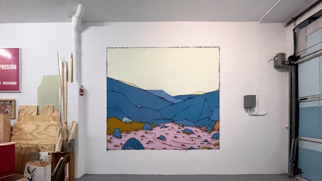 El mismo rincón de la nave con el mural Valle Peseta ya pintado en la pared: montañas azules, suelo rosa y cielo crema.