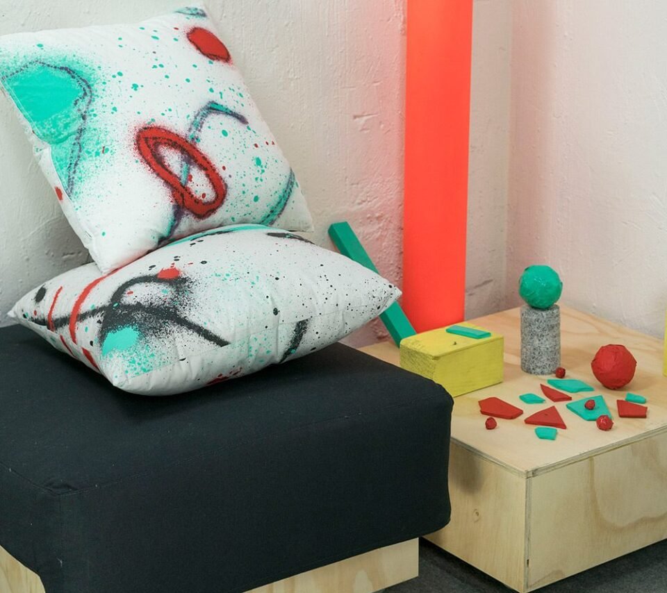 Cojines Discansa en un rincón, junto a un tubo naranja y piezas de madera pintadas