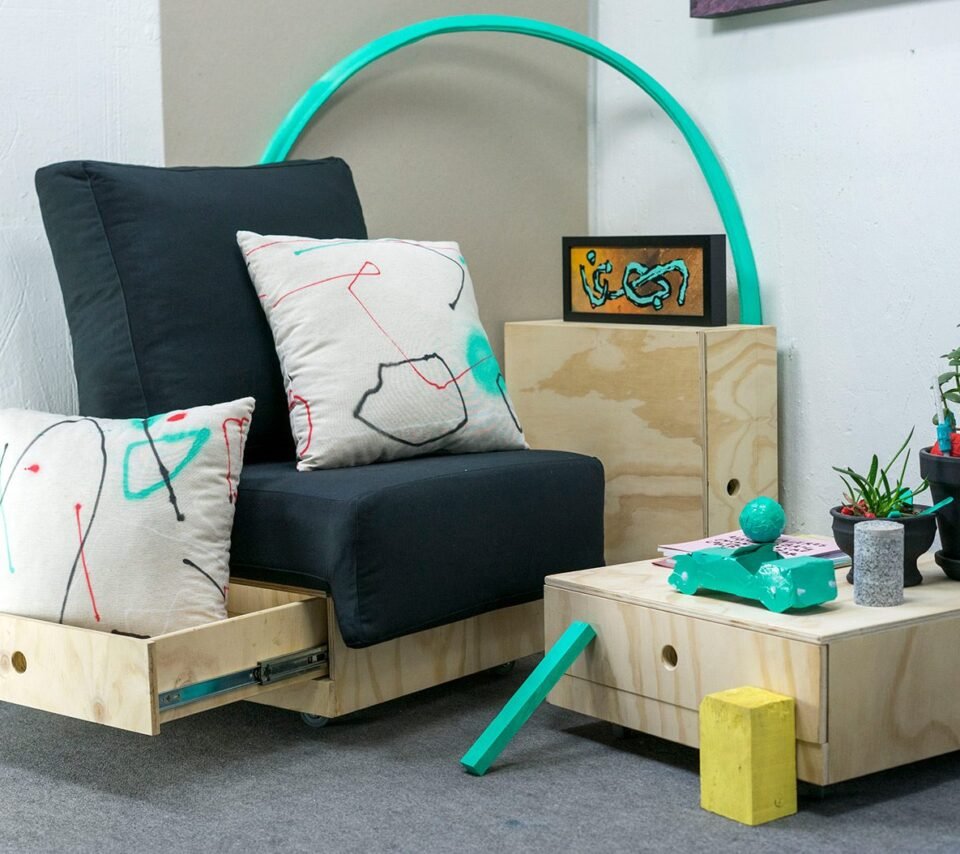 Conjunto de cojines Discansa en un salón, sobre un sillón negro, con obra de Sonek en la pared