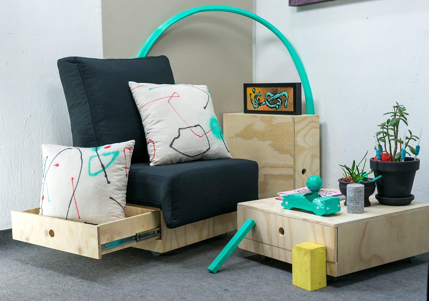 Conjunto de cojines Discansa en un salón, sobre un sillón negro, con obra de Sonek en la pared