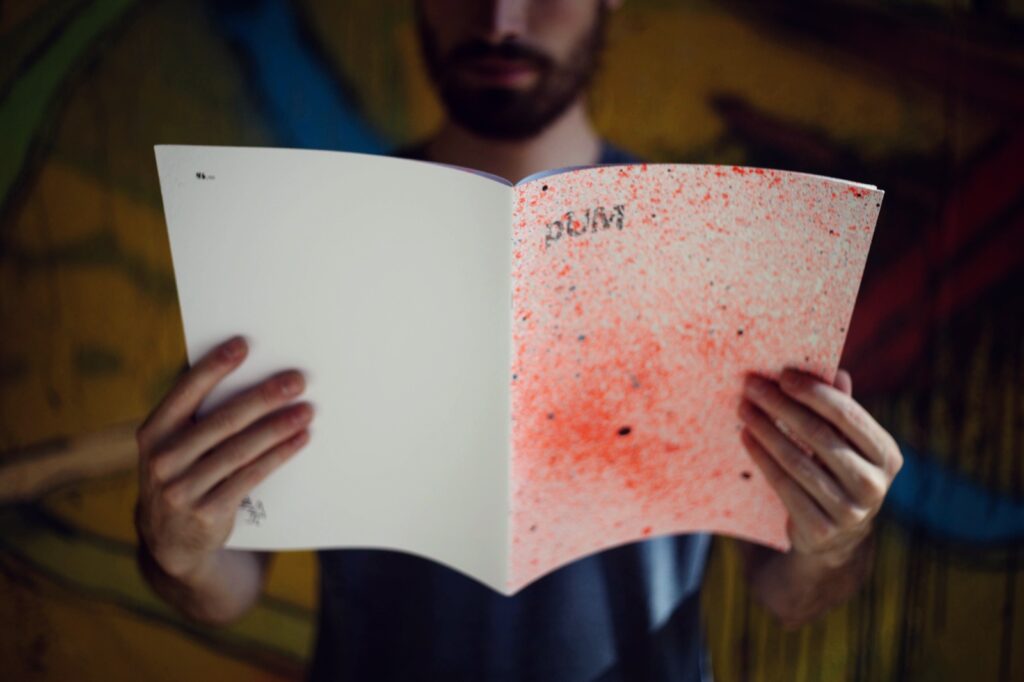 Fanzine Pum abierto entre las manos de un lector, frente a un muro pintado