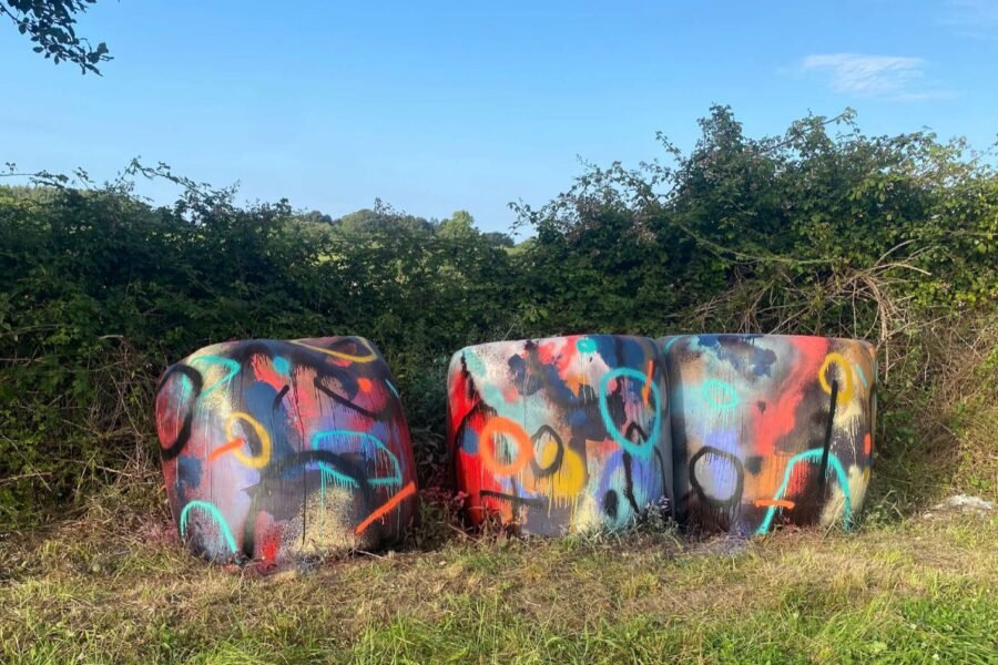 Tres bolas de silo pintadas por Sonek con círculos y colores vivos, en un prado asturiano