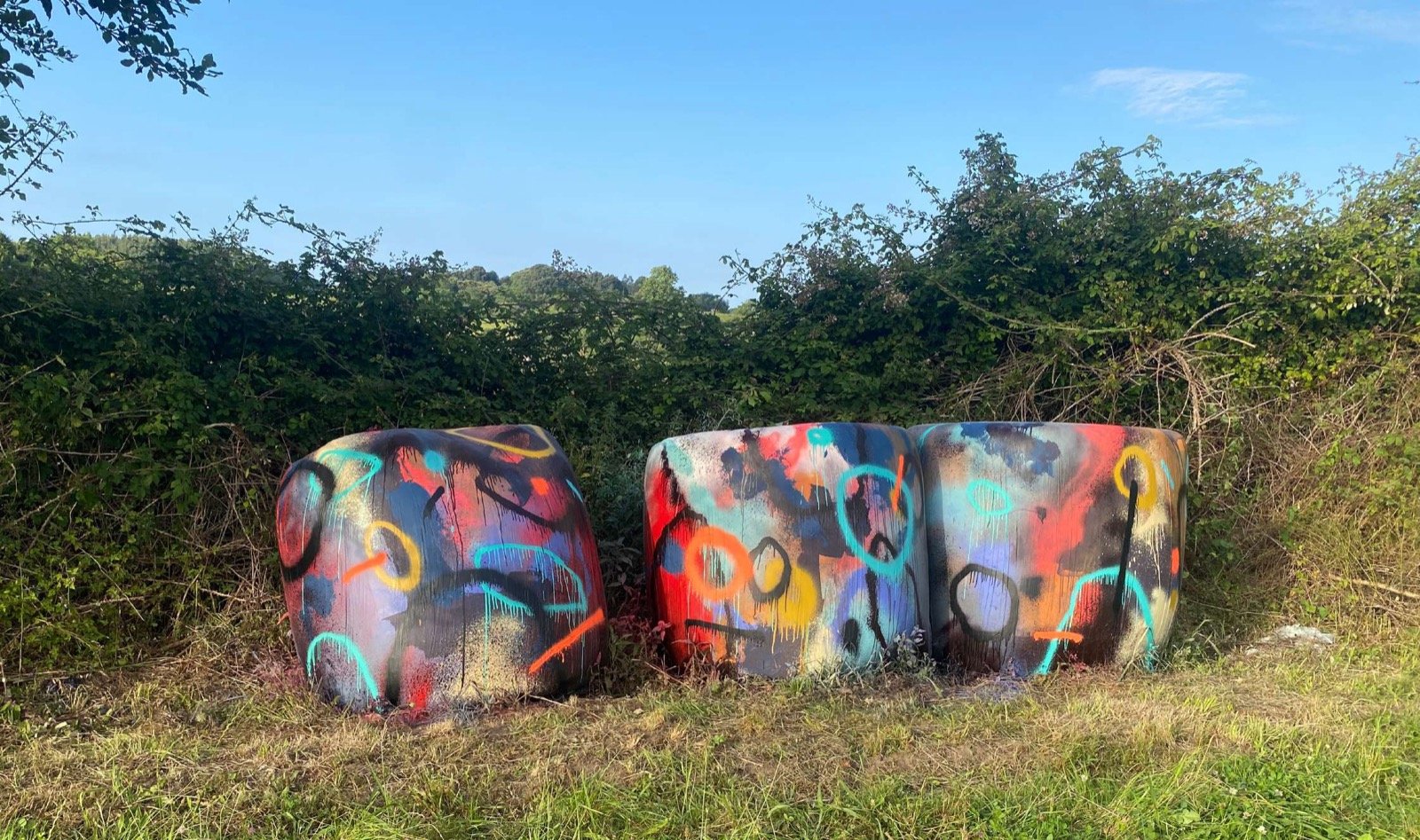 Tres bolas de silo pintadas por Sonek con círculos y colores vivos, en un prado asturiano