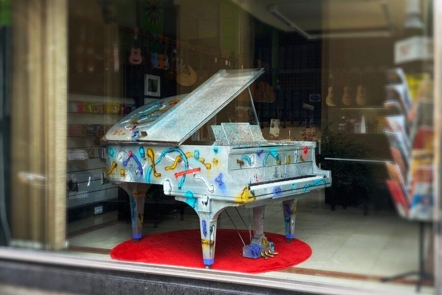 Piano de cola pintado por Sonek, visto desde la calle en el escaparate de una tienda de música