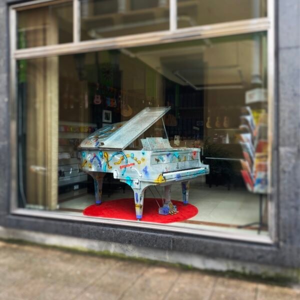 Piano de cola pintado por Sonek, visto desde la calle en el escaparate de una tienda de música