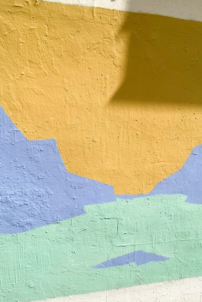 Detalle vertical de Al alba: el amarillo y el turquesa recién pintados sobre el muro.
