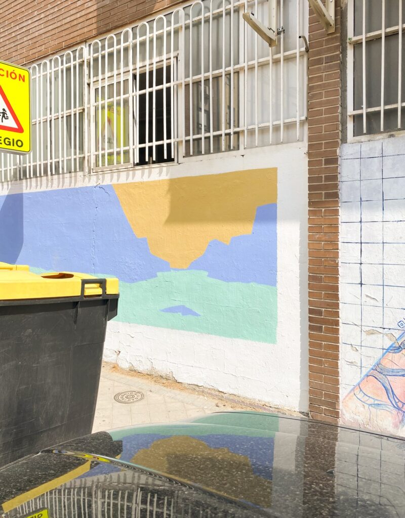 El muro de Al alba con los primeros bloques de azul, amarillo y turquesa, y contenedores delante.