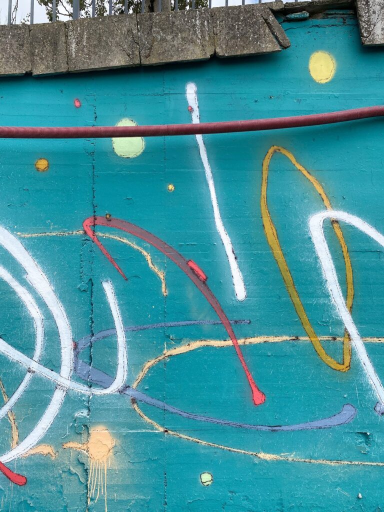 Detalle vertical del muro con lazos blancos, una elipse amarilla, un trazo rojo y puntos de color.