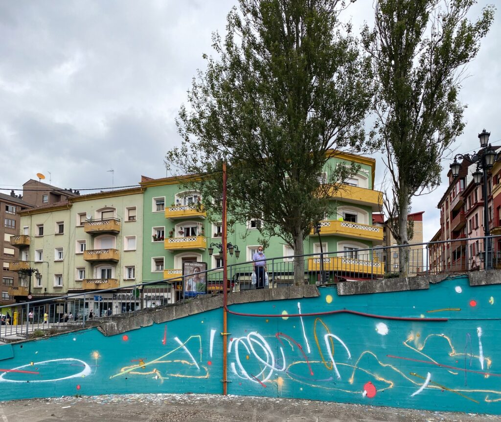 El muro turquesa terminado, con los álamos y los edificios de colores detrás.
