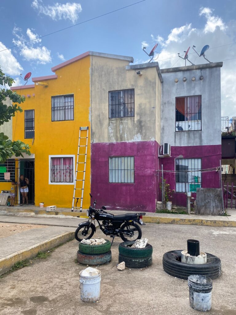 Las casas amarilla, gris y granate antes de pintar, con una moto y neumáticos pintados delante.