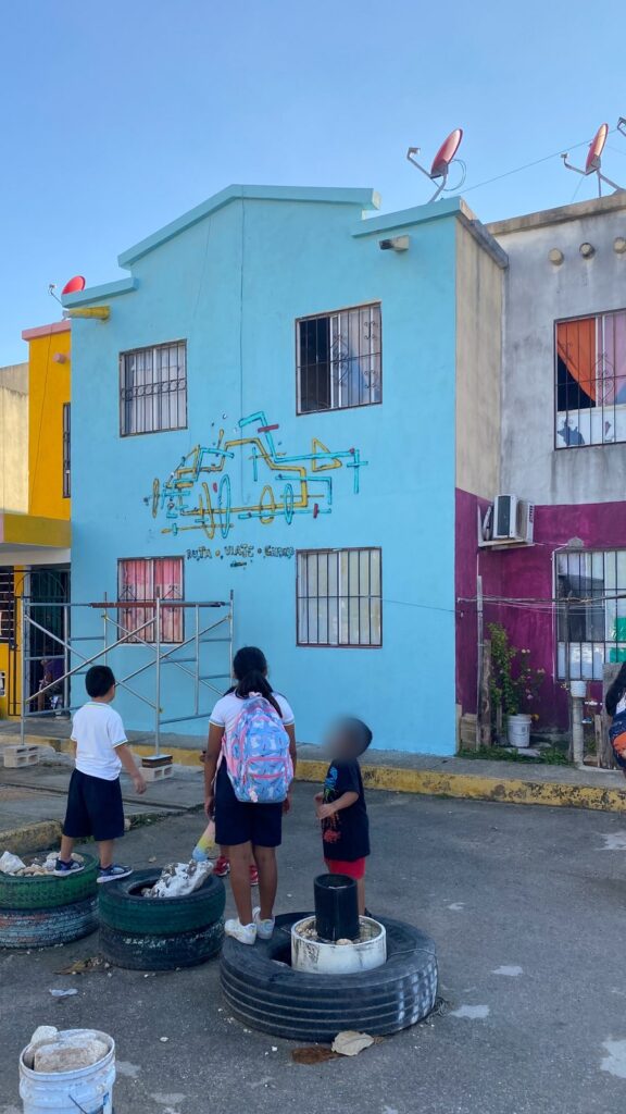 Tres niños con uniforme escolar miran el mural desde la calle, delante de la fachada con el andamio.