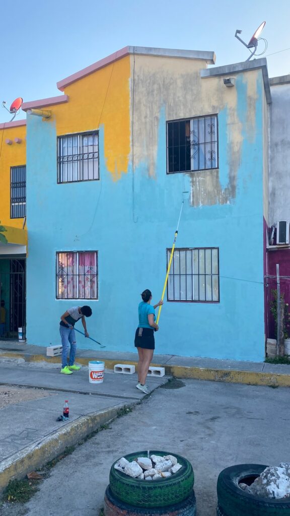 Dos personas pintan de azul con rodillo la fachada de la casa.