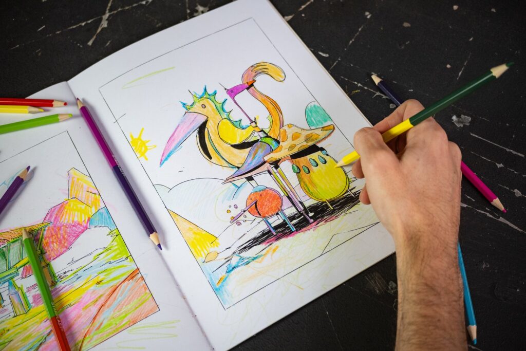 Una mano colorea con un lápiz amarillo un pájaro del cuadernillo, sobre una mesa negra con lápices de colores