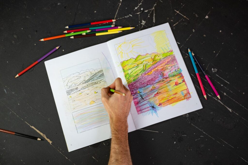 Una mano colorea un paisaje dibujado a línea; en la página de al lado, otro paisaje ya coloreado en colores intensos