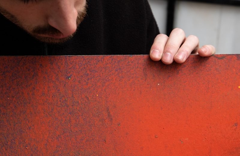 Sonek mirando de cerca una tabla pintada en rojo anaranjado, en su taller de Madrid